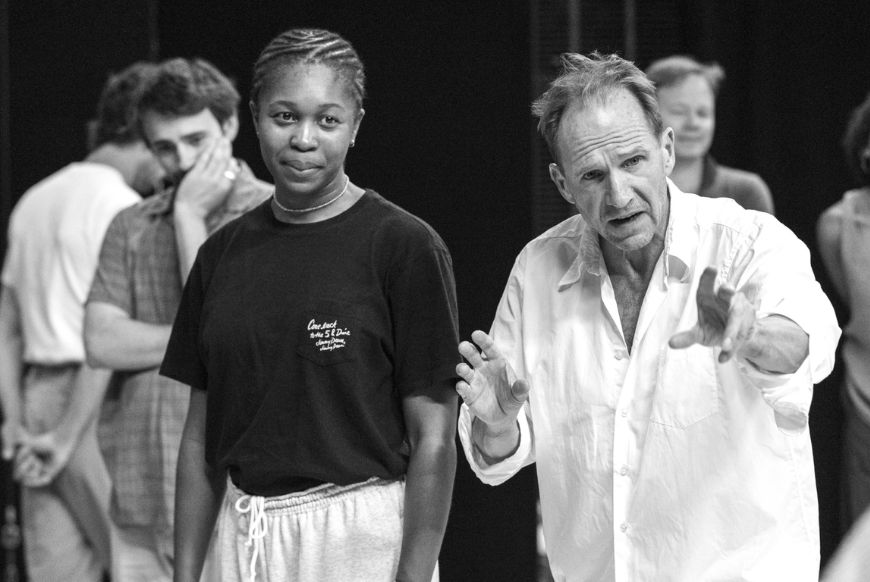 black and white image of actor ralph fines on stage with several other actors, during a scene